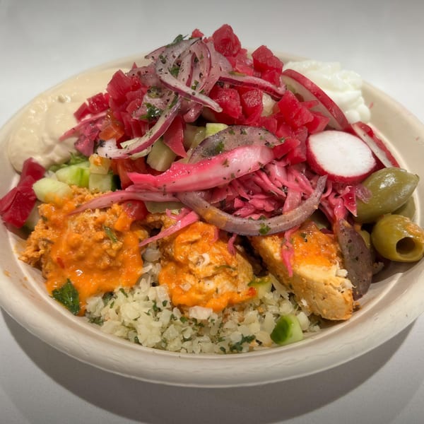 A vibrant Middle Eastern bowl with cauliflower rice, chicken, hummus, pickled vegetables, and olives.
