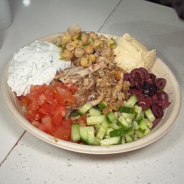 A Nana Street Food bowl with chicken, hummus, tzatziki, chickpeas, tomatoes, cucumbers, and olives.