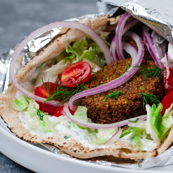 Nana Street Food's falafel wrap with red onions, tomatoes, lettuce, and sauce, partially wrapped in foil.
