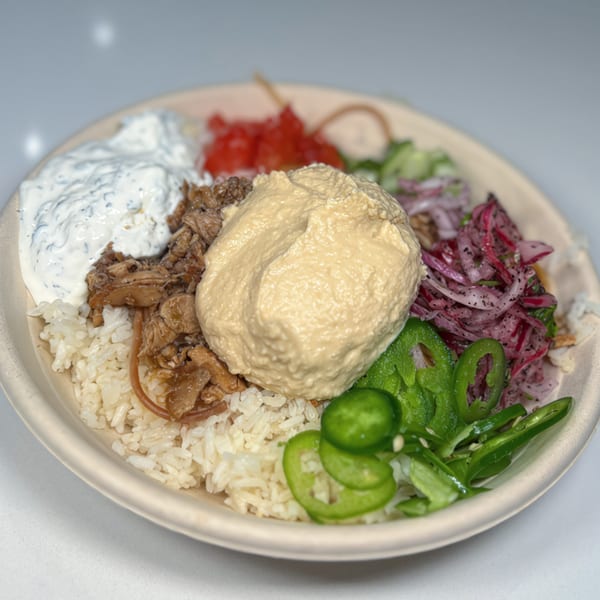 Middle-Eastern rice bowl with chicken, hummus, tzatziki, pickled onions, and sliced green chilies.