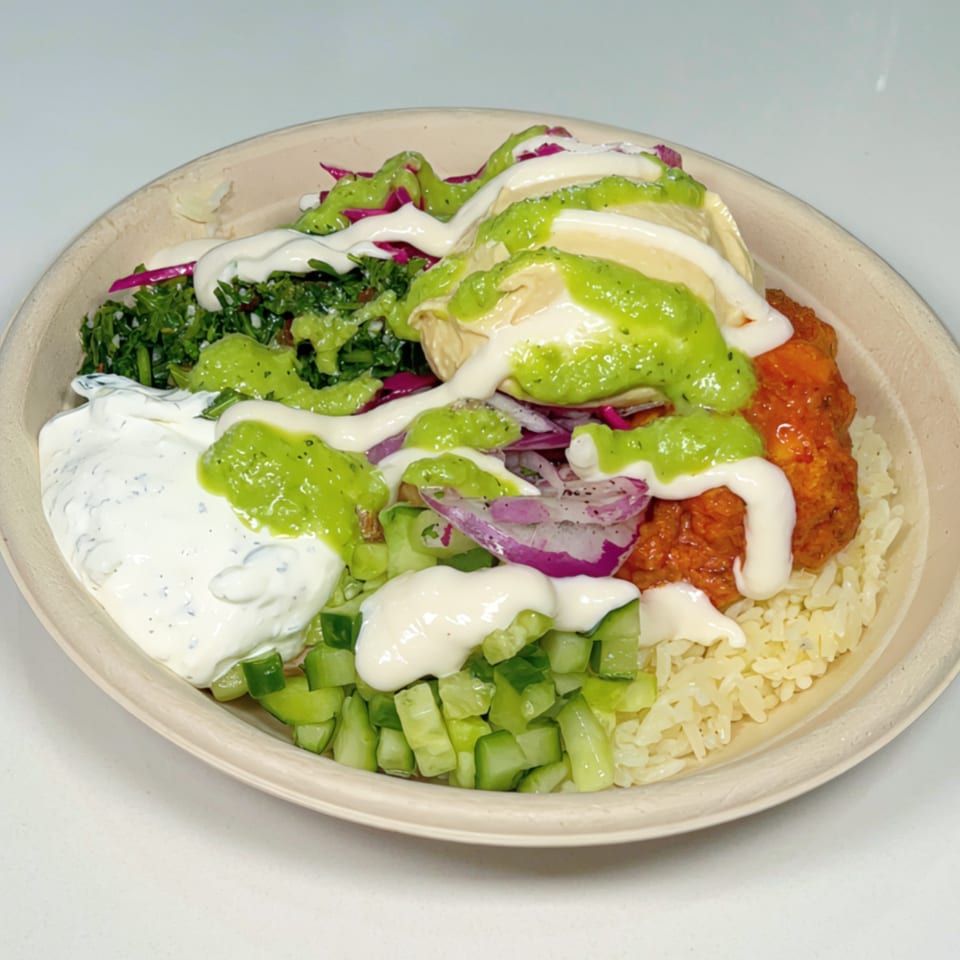A vibrant Nana Street Food bowl with rice, chicken, hummus, tabbouleh, cucumbers, and sauces.