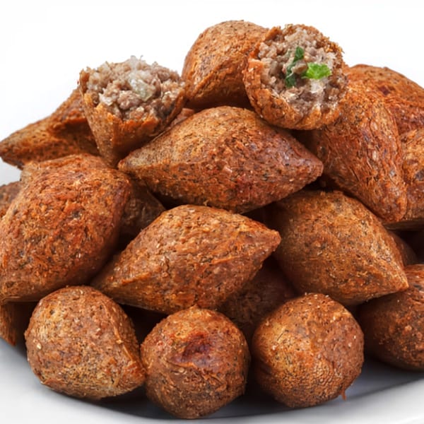 A pile of golden-brown Nana Street Food kibbeh, some revealing their savory meat and herb filling.