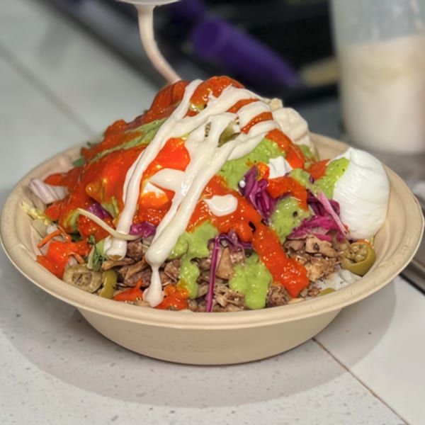 A Nana Street Food bowl with meat, vegetables, red sauce, green sauce, and white sauce.