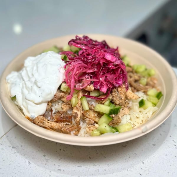 Middle-eastern chicken and rice bowl with white sauce, pickled red cabbage, and diced cucumbers.